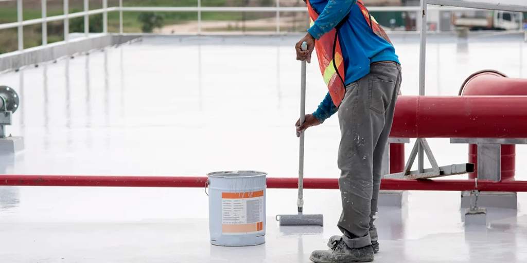 A worker applying elastomeric roof coating to a mobile home roof with a paint roller.