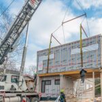 Modular home under construction in snowy Canadian landscape with crane installing roof section