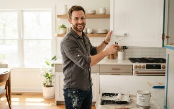 A man using a roller to paint modern kitchen cabinets white.